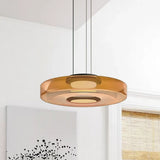 Single amber glass disc pendant light against a near-plain white wall with art