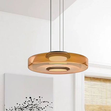Single amber glass disc pendant light against a near-plain white wall with art