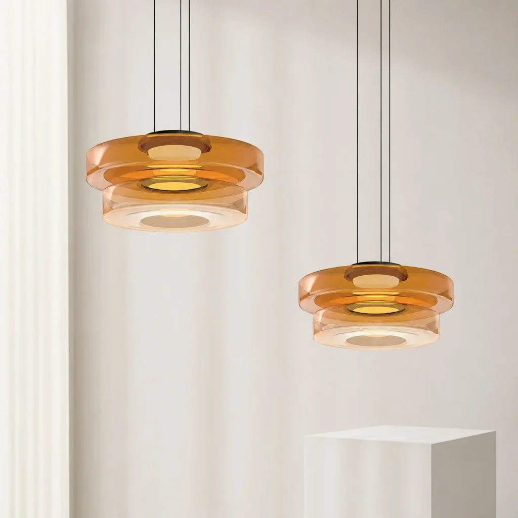 Two amber three-layer glass pendant lights on a pale studio-white plinth