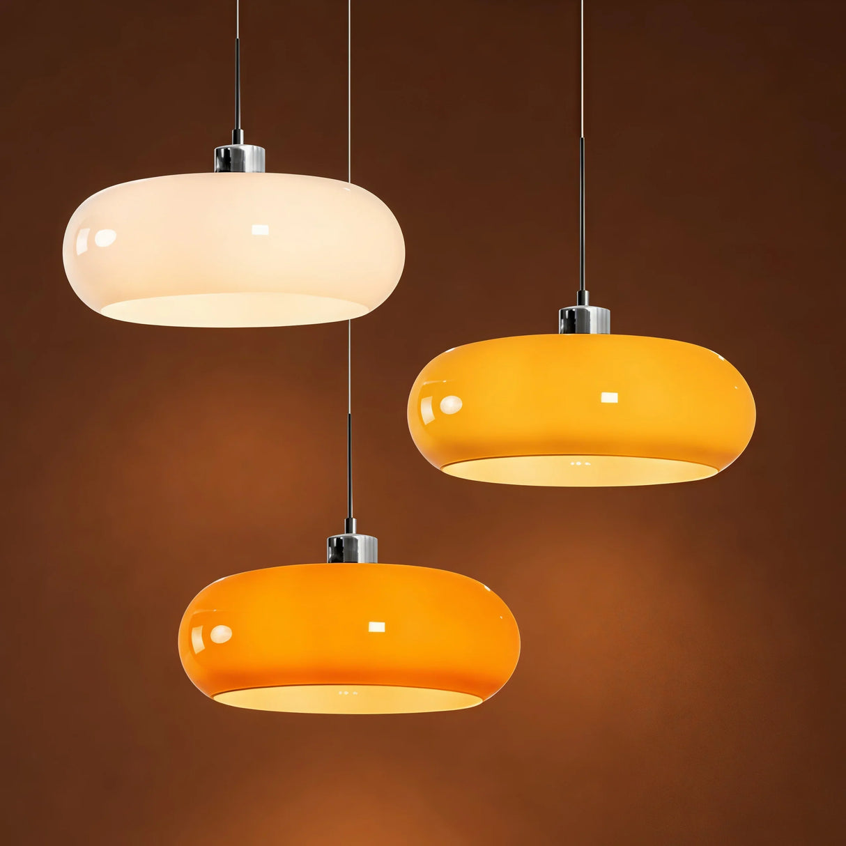 White, orange, and amber glass pendant light trio on brown studio backdrop