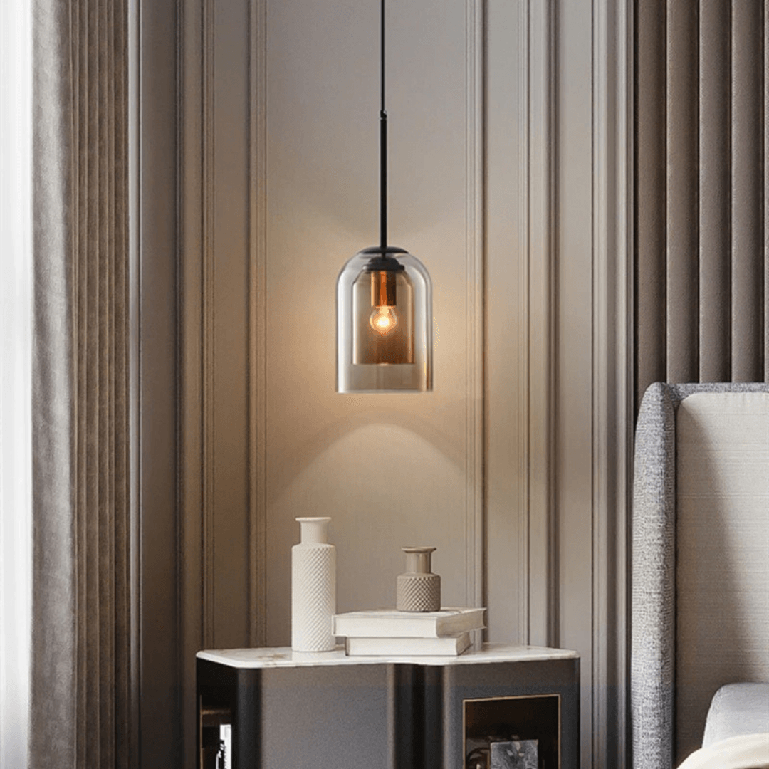 Double glass pendant lit warm beside a bed and side table