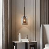 Double glass pendant lit warm beside a bed and side table