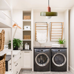 Olive glass pendant light lighting a white laundry room with drying racks
