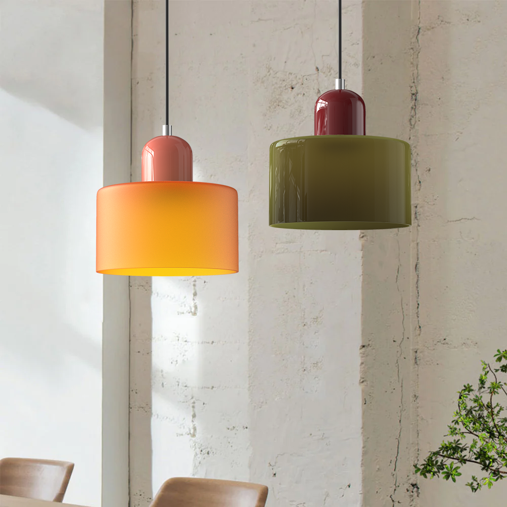 Orange and green glass pendant lights hanging over a table by a brick wall
