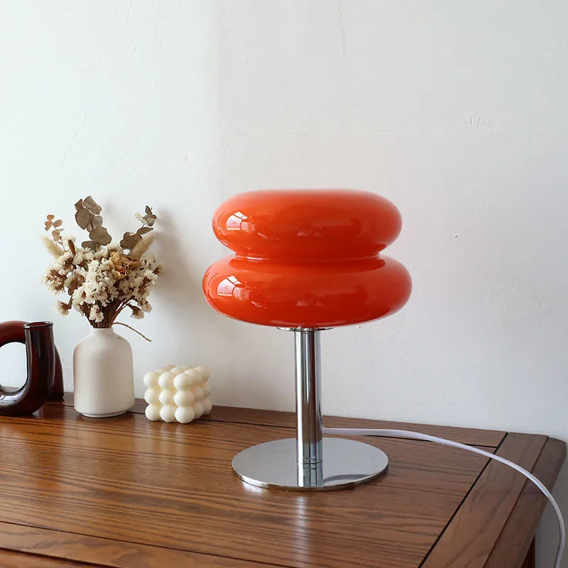 Deep orange glass lamp glowing on a wooden sideboard by a white wall