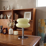 Pale yellow stacked lamp lit on a wooden cabinet beside pottery