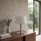 White stacked glass lamp lit on a console table beside a doorway