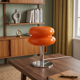 Orange stacked glass table lamp lit on a wooden desk by a window