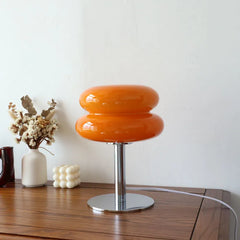 Orange two tier glass lamp lit beside dried flowers on a sideboard