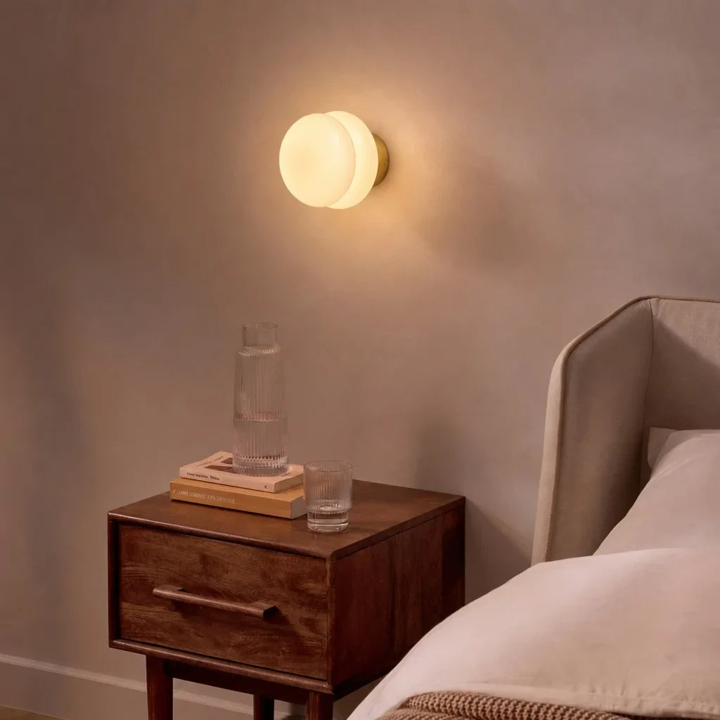 Warm glass wall sconce glowing above a walnut bedside nightstand