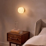 Warm glass wall sconce glowing above a walnut bedside nightstand