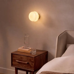Warm glass wall sconce glowing above a walnut bedside nightstand