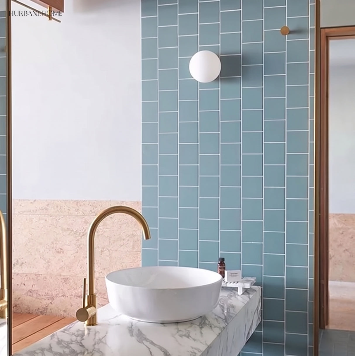 Glass globe wall light on blue tiled bathroom wall above a marble basin