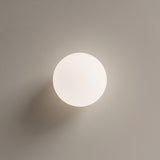 White glass globe ceiling light with gold base on a plain wall