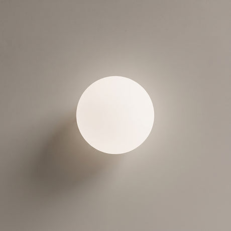 White glass globe ceiling light with gold base on a plain wall