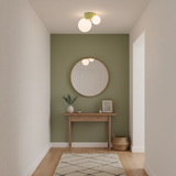 Twin globe ceiling light above a sage green wall with a round mirror below