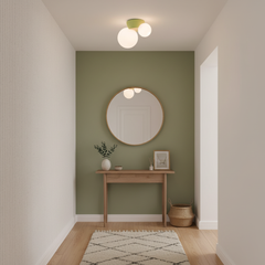 Twin globe ceiling light above a sage green wall with a round mirror below
