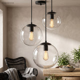 Two glass globe pendants lit above a dining table and rattan chair