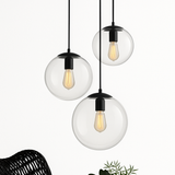Three glass globe pendants lit above a woven chair and plant