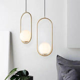 Two gold hoop pendants hanging against a white wall beside a plant