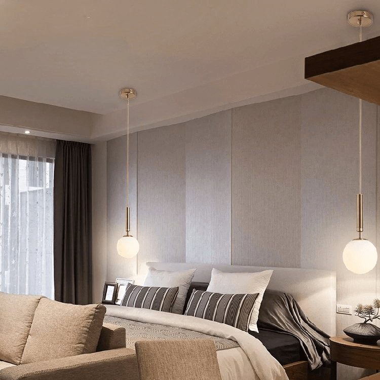 Two brass globe pendants lit either side of a bed in a beige bedroom