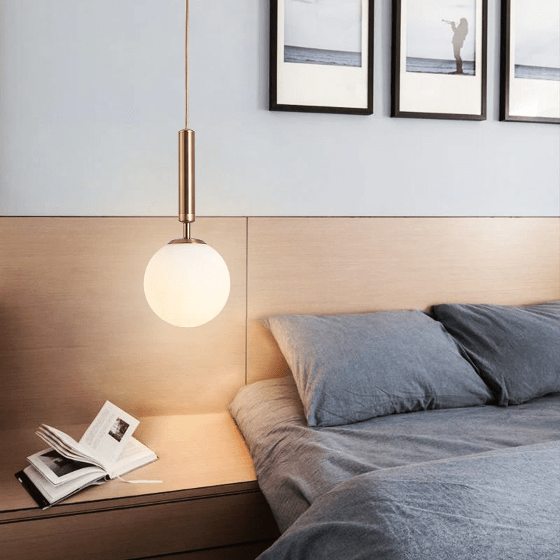 Brass globe pendant lit above a wooden bedside table and open book