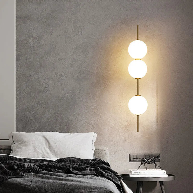 Three opal globes lit beside a bed with a dark grey throw