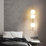 Three opal globes lit beside a bed with a dark grey throw
