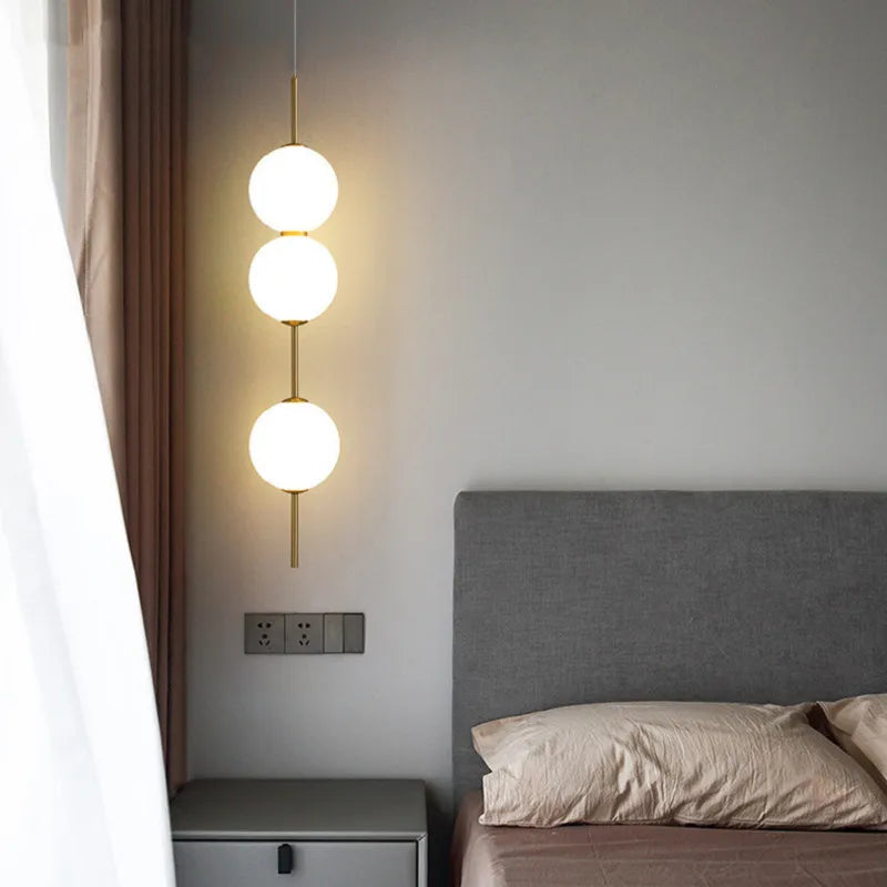 Three stacked opal globes lit beside a bed and pale curtain