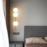 Three stacked opal globes lit beside a bed and pale curtain