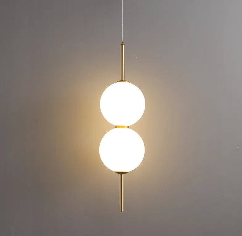 Two lit opal globes on a brass rod against a plain grey wall