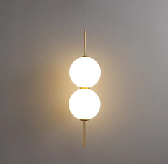 Two lit opal globes on a brass rod against a plain grey wall