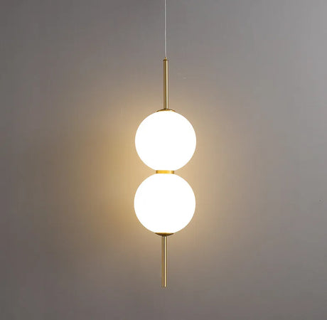 Two lit opal globes on a brass rod against a plain grey wall