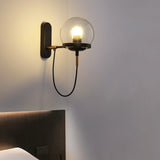 Brass globe wall sconce lit close beside a dark upholstered headboard