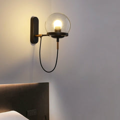 Brass globe wall sconce lit close beside a dark upholstered headboard