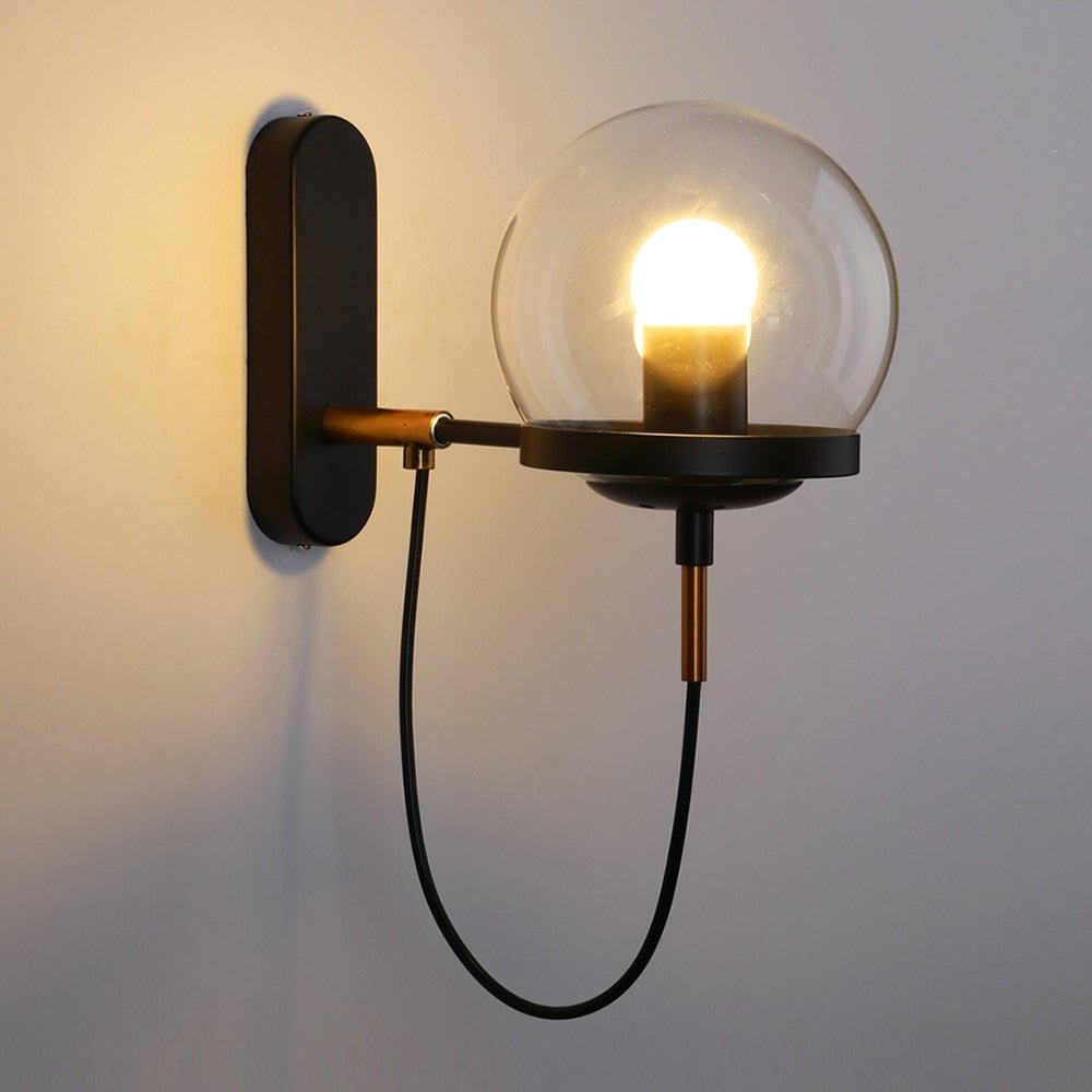 Black globe wall sconce lit warmly against a plain pale wall