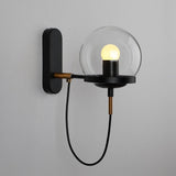 Black wall sconce with a clear glass globe lit on a white wall
