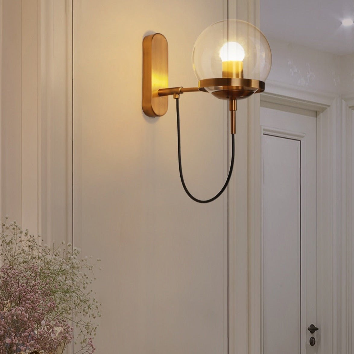 Brass globe wall sconce lit on a pale wall beside a panelled door