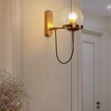Brass globe wall sconce lit on a pale wall beside a panelled door