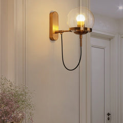 Brass globe wall sconce lit on a pale wall beside a panelled door