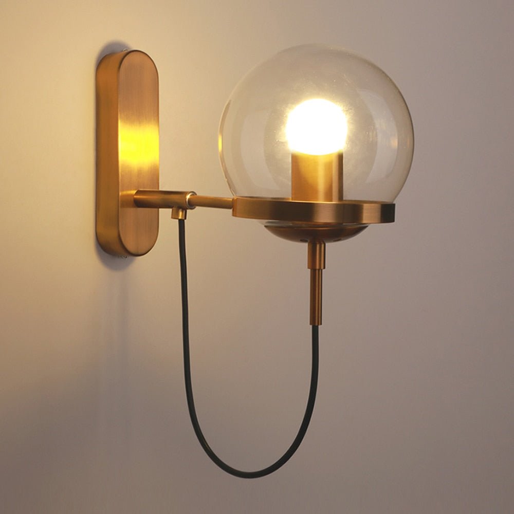 Brass wall sconce with a clear glass globe and a looped cord below