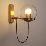 Brass wall sconce with a clear glass globe and a looped cord below