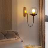 Brass globe wall sconce lit beside a tall mirror and a padded headboard