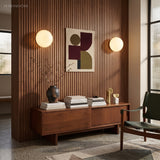 Two globe wall sconces flanking abstract art on a walnut slat wall