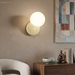 Wall sconce with an opal globe lit above a walnut sideboard and a boucle chair