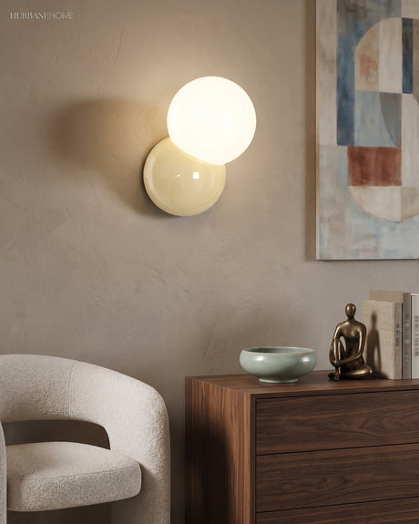 Wall sconce with an opal globe lit above a walnut sideboard and a boucle chair