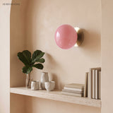 Pink glass globe sconce with gold scalloped plate above a shelf