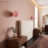 Two pink globe sconces flanking a bed with timber nightstands
