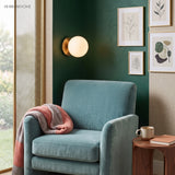 Globe wall sconce on green wall above a teal armchair and prints