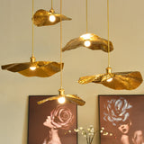 Gold lotus leaf pendant light glowing above framed rose prints on a wall